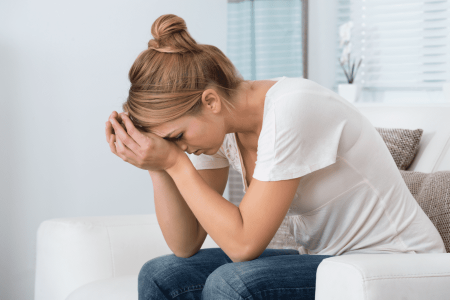 A woman sits on a white couch with her head in her hands